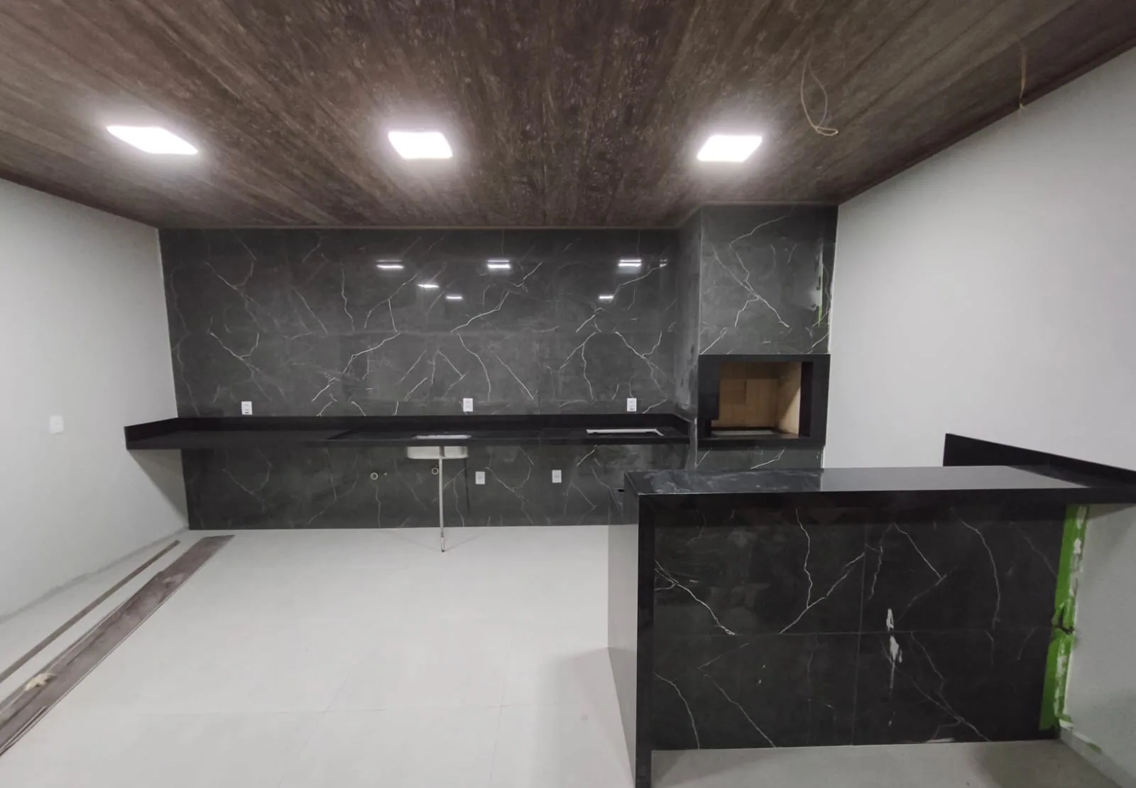 Area gourmet revestida em marmore preto com veios brancos, bancada e ilha em pedra macica