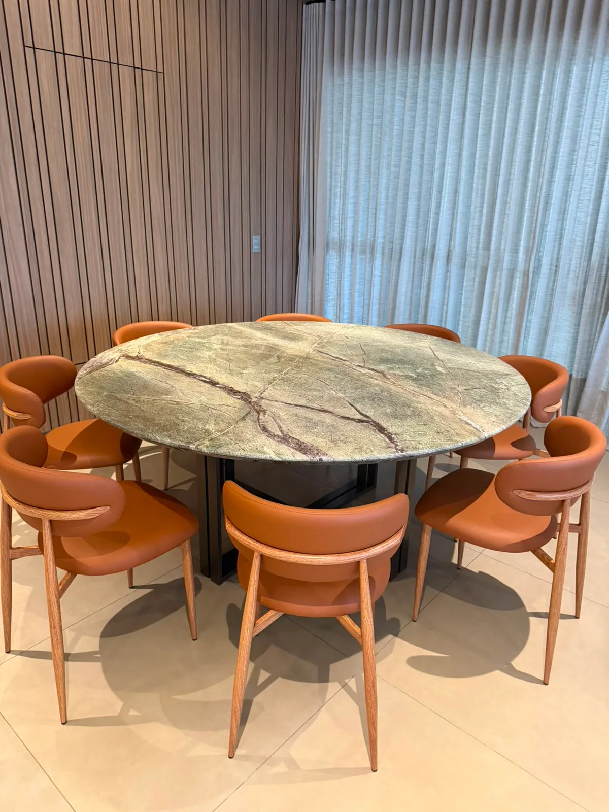 Sala de jantar com mesa redonda em pedra exotica, painel ripado de madeira e cortinas em linho